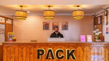 A reception desk with a 'PACK' sign, a man standing behind it, and three hanging lamps.