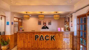 Mostrador de recepción con el rótulo 'PACK', acabado de madera, tres lámparas colgantes y una recepcionista.