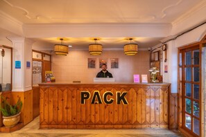 A reception desk labeled 'PACK' with a wooden finish, three hanging lamps, and a receptionist. - Kalra Regency Shimla (Shimla)