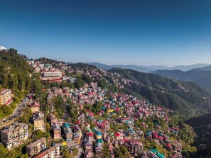 A hillside town with densely packed buildings, a prominent multi-story hotel, and a clear view of the surrounding mountains. - Kalra Regency Shimla (Shimla)
