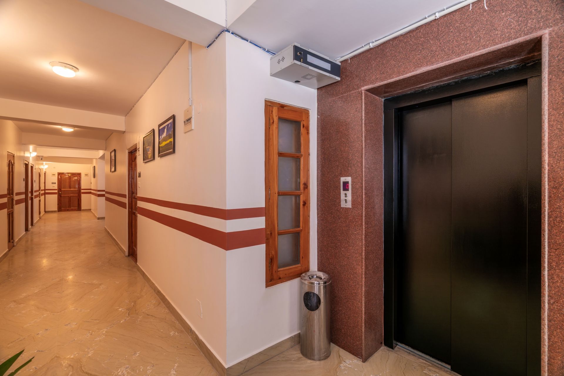 Un couloir d’hôtel avec un sol en marbre, une poubelle, un ascenseur et une porte dotée d’un panneau en verre dépoli.