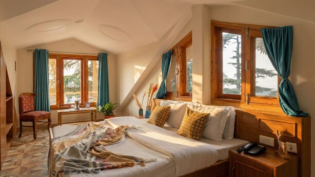 Un dormitorio con una cama, una silla, un escritorio y ventanas con cortinas.