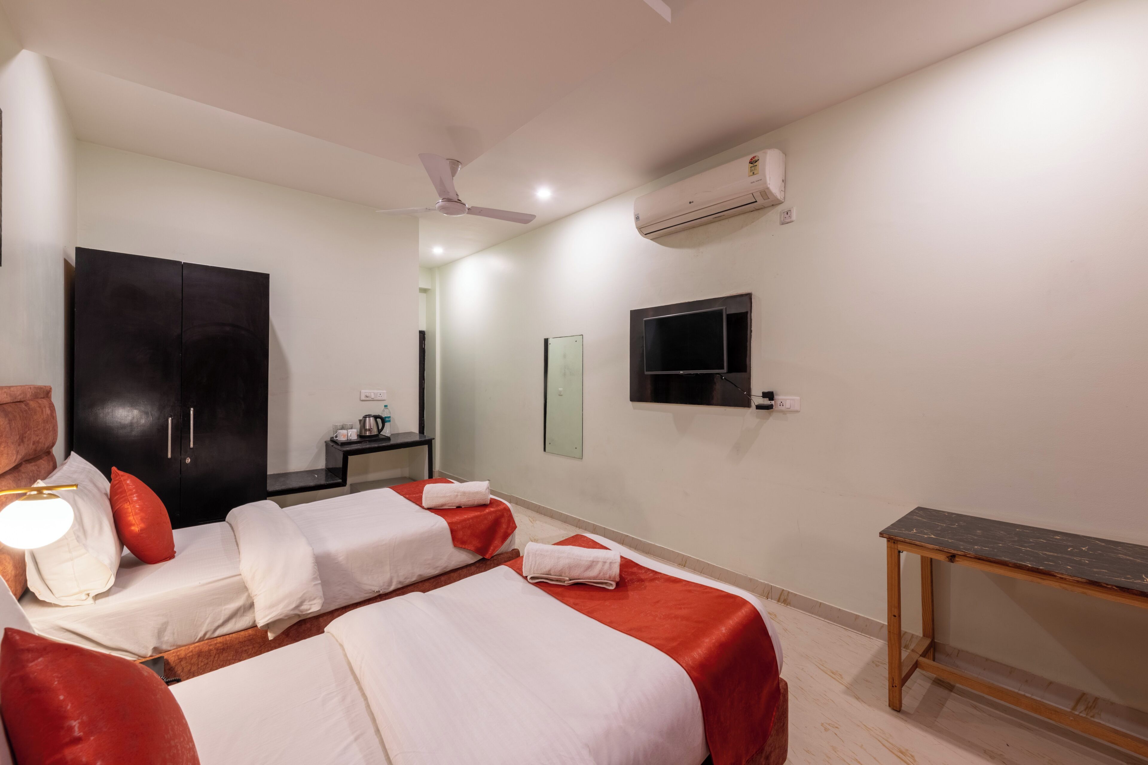 A hotel room with two beds, a desk, a ceiling fan, an air conditioner, and a TV mounted on the wall.