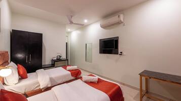 A hotel room with two beds, a desk, a ceiling fan, an air conditioner, and a TV mounted on the wall.