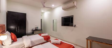 A hotel room with two beds, a desk, a ceiling fan, an air conditioner, and a TV mounted on the wall.