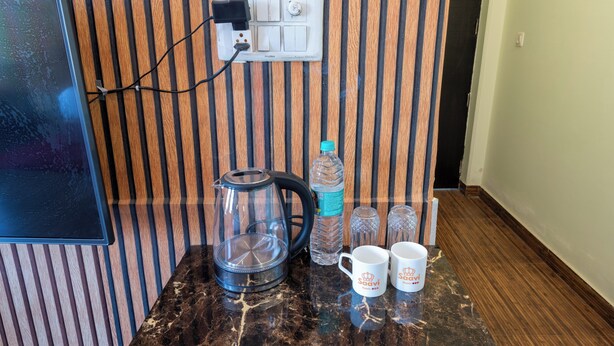 A kitchen counter with a coffee maker, water bottle, and two coffee mugs. - La Comfort By shrpl (Gurugram)