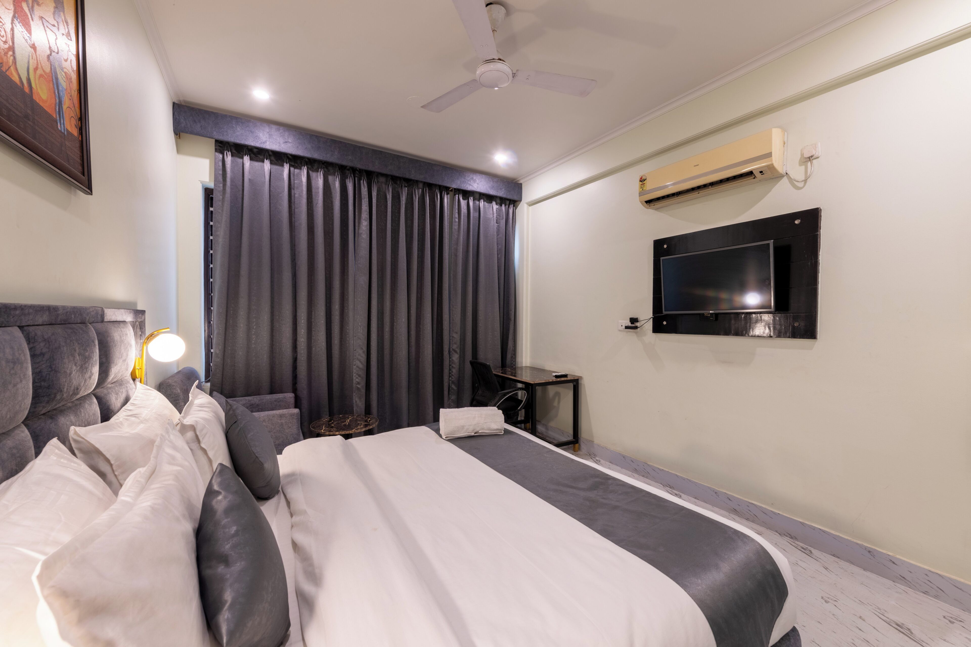 A hotel room with a bed, a desk, a chair, a television, and a ceiling fan.