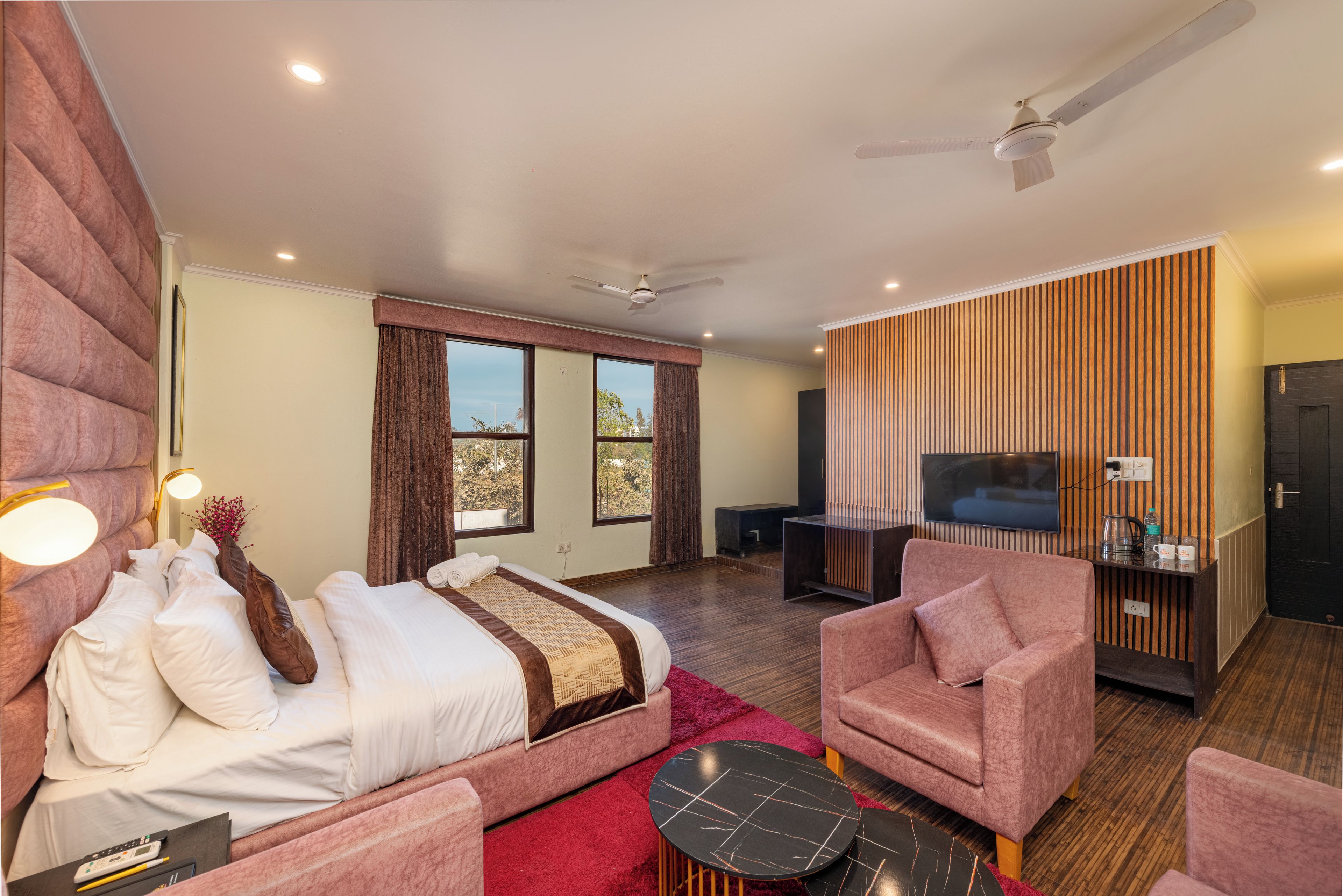 A modern hotel room with a sofa bed, a separate armchair, a flat-screen TV, and a ceiling fan.