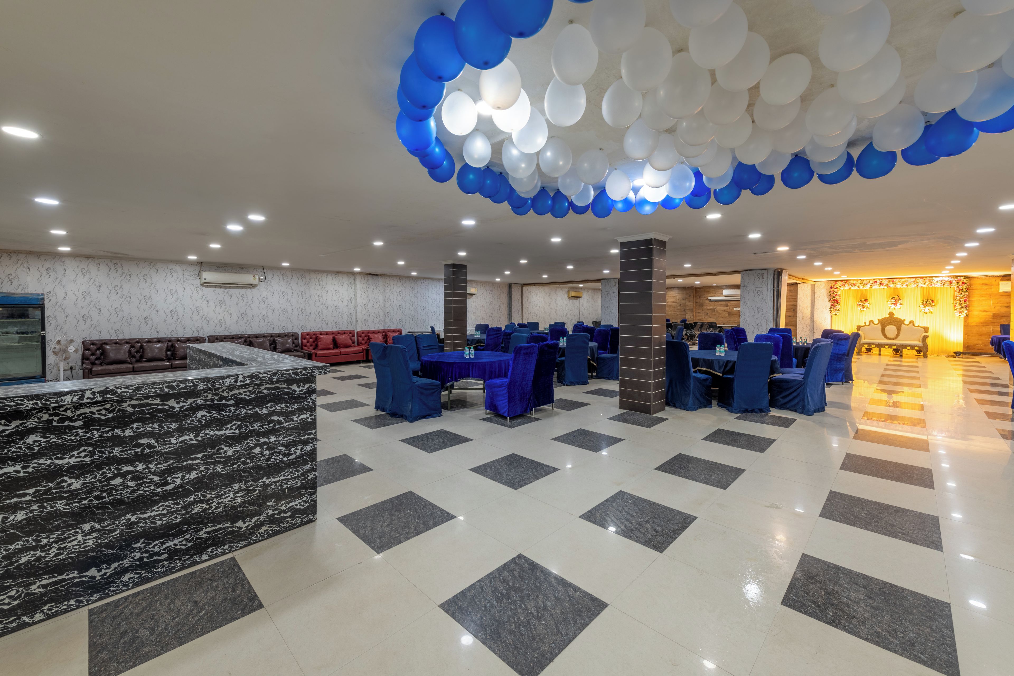 A spacious indoor area with a checkered floor, multiple tables with chairs, and a ceiling adorned with balloons.