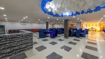 A spacious indoor area with a checkered floor, multiple tables with chairs, and a ceiling adorned with balloons.
