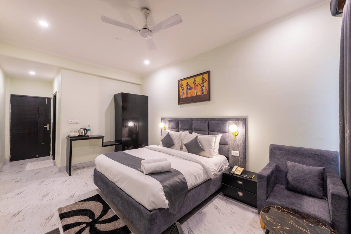A bedroom with a bed, bedside tables, a chair, a desk, a wardrobe, a ceiling fan, and a painting on the wall.