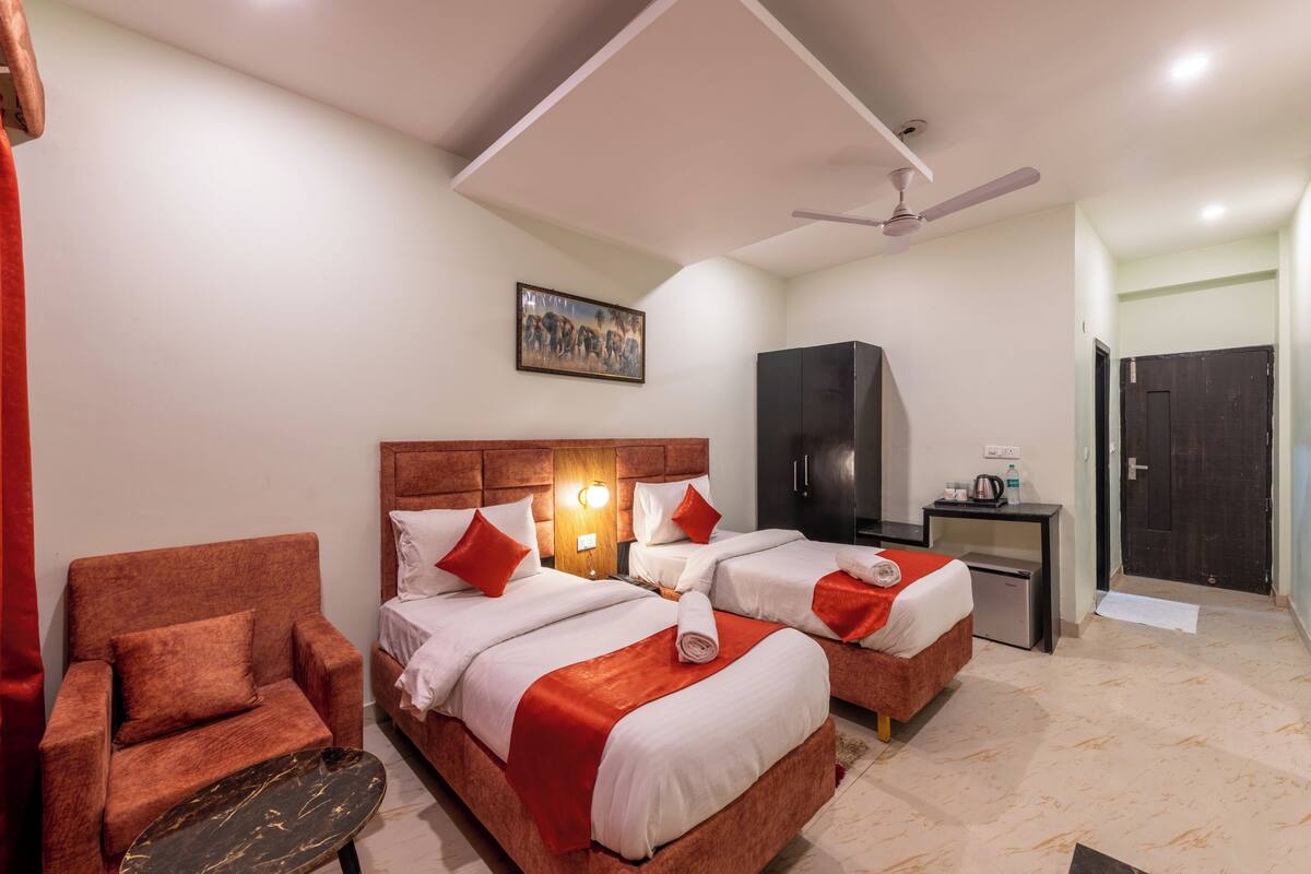 A hotel room with two beds, a chair, a desk, a wardrobe, and a ceiling fan.