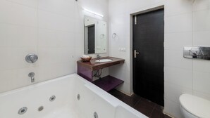 A bathroom with a bathtub, a sink, a mirror, a toilet, and a door. - La Comfort By shrpl (Gurugram)