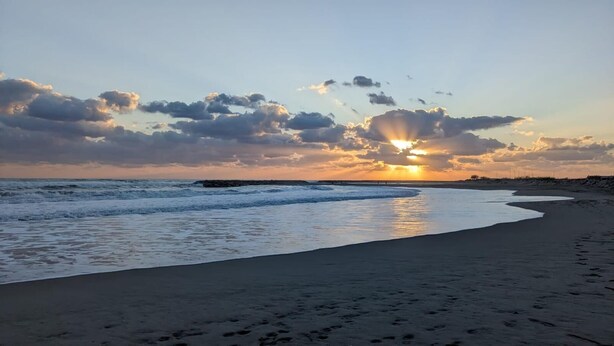 Uma praia com pôr do sol, ondas e céu claro.