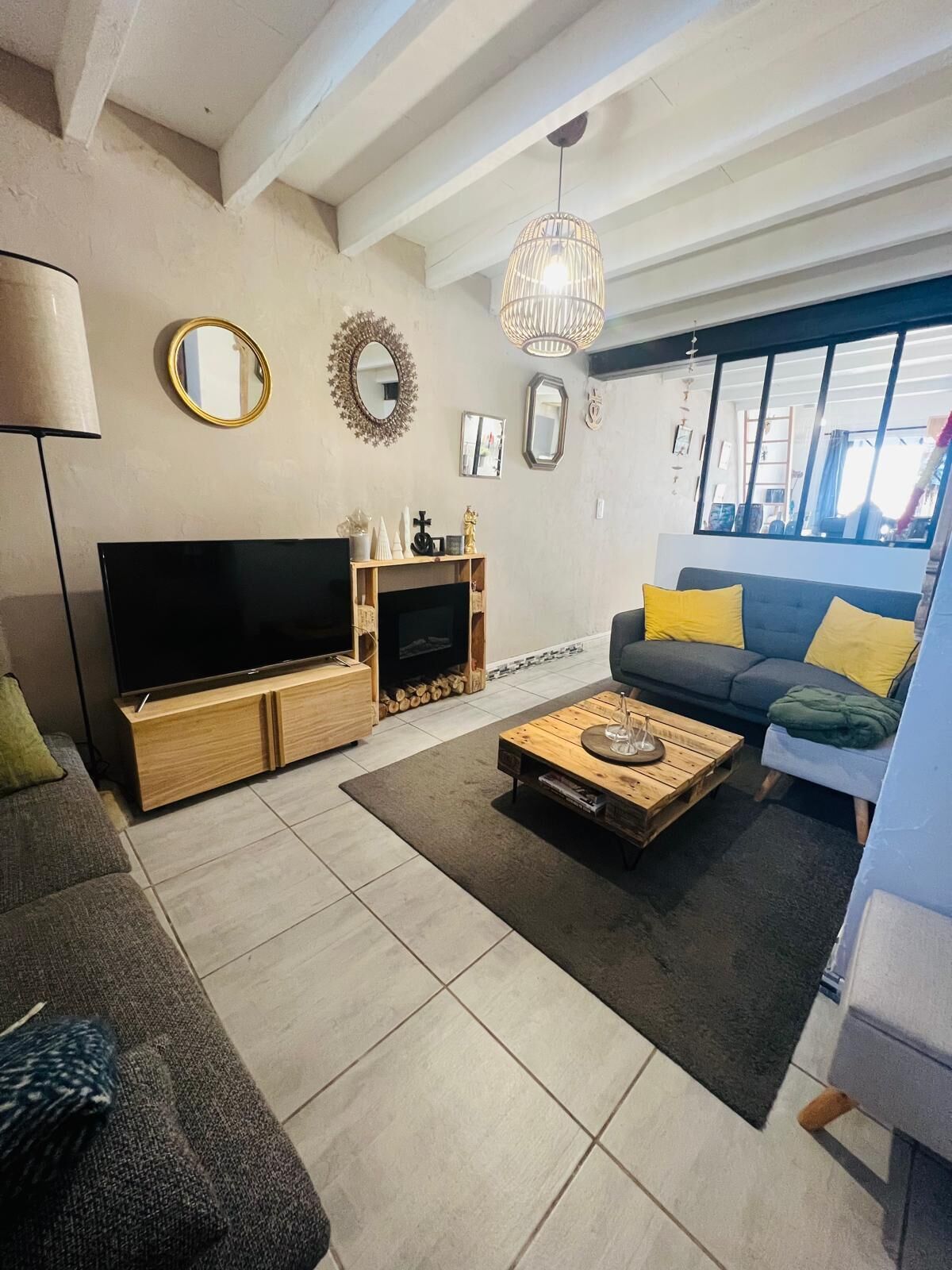 A living room with a TV, sofa, coffee table, fireplace, and large windows.