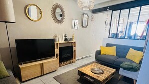 Sala de estar com televisão, sofá, mesa de centro, lareira e grandes janelas.