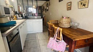 Cozinha compacta com eletrodomésticos modernos, área de jantar com cadeiras de vime e vista através de uma grande janela.