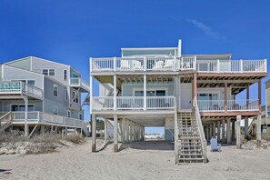 Ein mehrstöckiges Gebäude direkt am Strand mit Balkonen, einer Treppe und einem Liegestuhl.