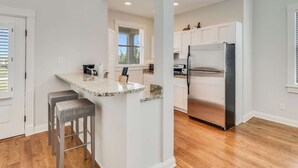 A modern kitchen with a central island, stainless steel refrigerator, and white cabinetry. - OBX Beach House + Pools. Sunsets & Ocean Path (Duck)