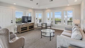A spacious living room with a television, seating area, and large windows. - OBX Beach House + Pools. Sunsets & Ocean Path (Duck)