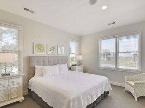 A bedroom with a large bed, a nightstand, a chair, and artwork on the wall.