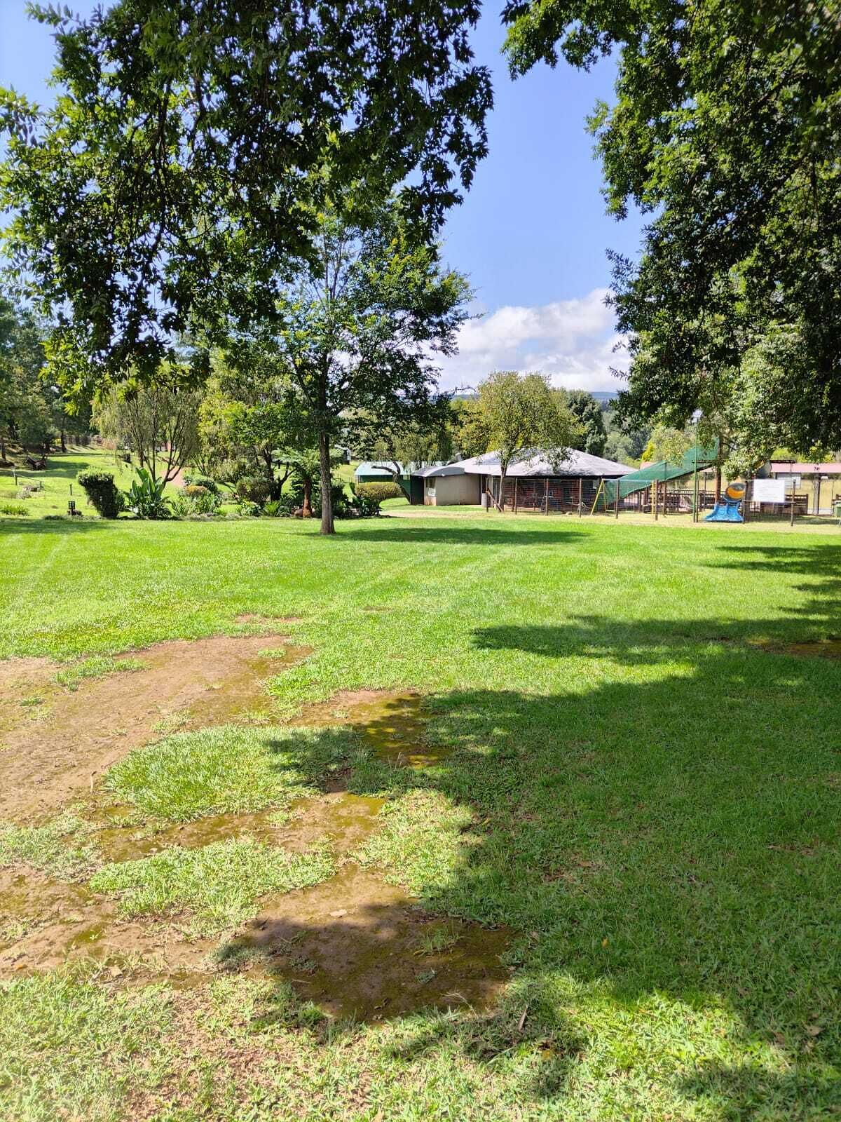 A grassy outdoor area with trees, a building, and a playground.