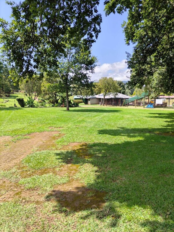 A grassy outdoor area with trees, a building, and a playground. - Sabie River Camp (Sabie)