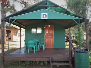 Una pequeña estructura con techo verde, puerta de madera y una mesa con sillas.