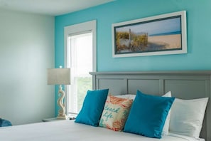 A bedroom with a bed, a nightstand, a lamp, a window, and a painting on the wall.