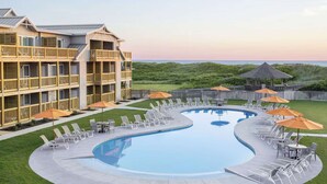 Un espace piscine avec des chaises longues et des parasols, un bâtiment doté de balcons et une vue sur l’océan.