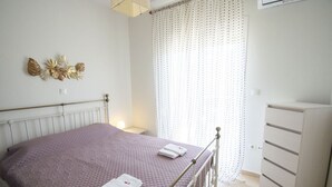 Ein Schlafzimmer mit einem Bett, einem Nachttisch, einer Kommode und einem Fenster mit Vorhängen.