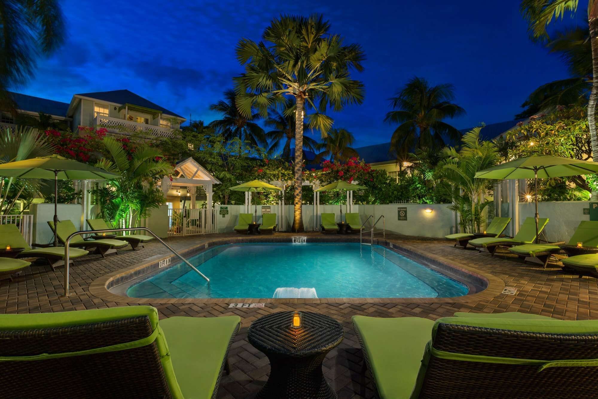A pool area with lounge chairs, a hot tub, and palm trees.