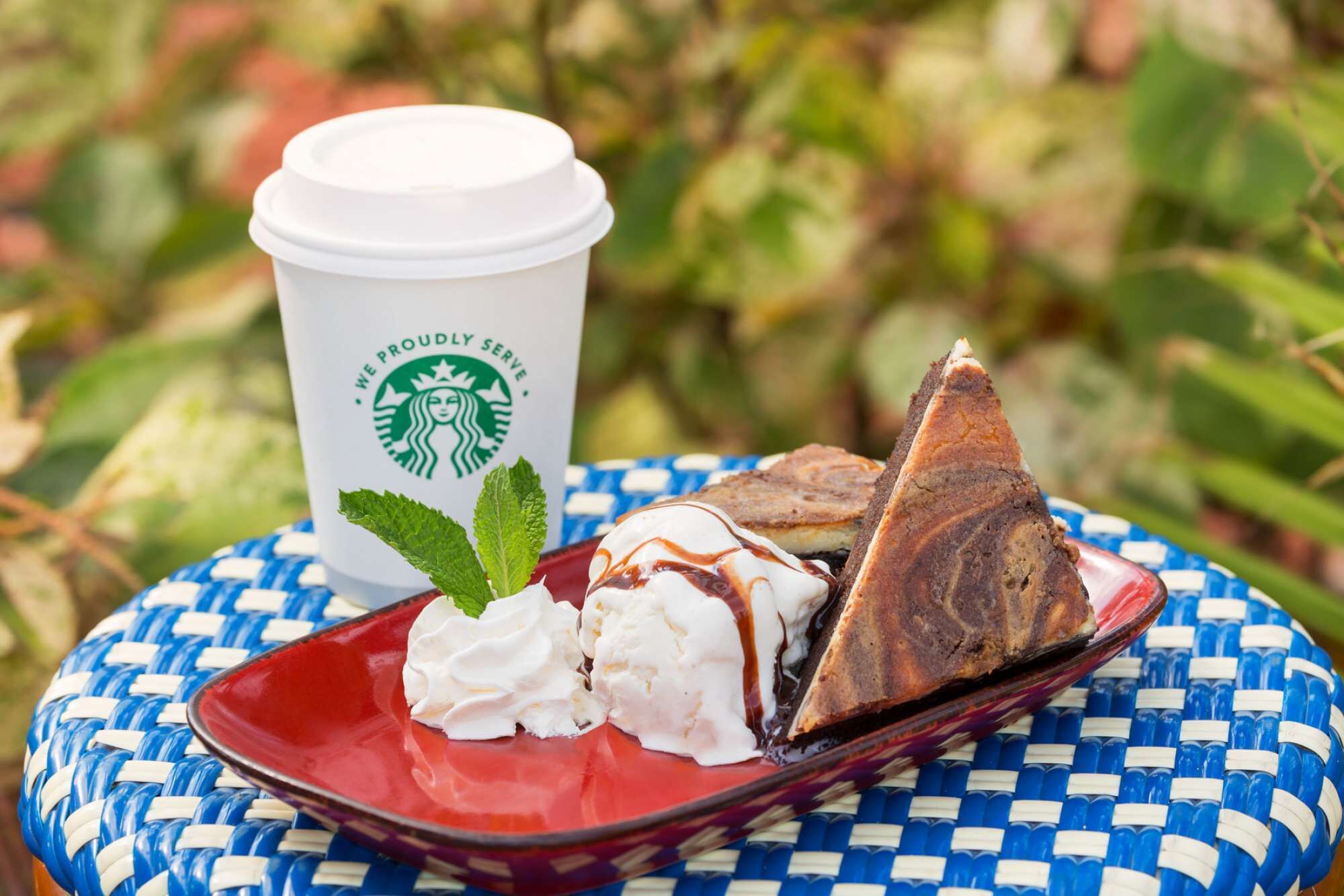 Eine Starbucks-Tasse, Schlagsahne und ein Stück Kuchen auf einem gewebten Tisch.