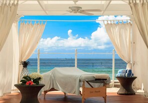A massage table with a towel, a wicker table with flowers, and a view of the ocean. - Beachfront Key West + Free Breakfast, Pool & Spa (Key West)