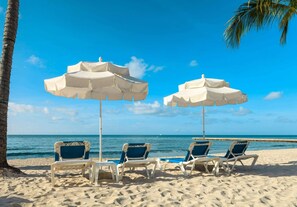 A beach with two white umbrellas and three blue chairs. - Duval Street Stay + Free Breakfast, Beach & Pool (Key West)
