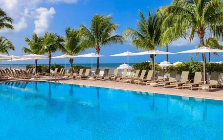 A pool with lounge chairs and umbrellas, palm trees, and a clear sky.