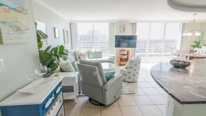 Ein modernes Wohnzimmer mit Sofa, Essbereich, Fernseher und großem Fenster mit Blick auf die Stadt.