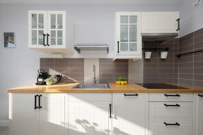 A kitchen with white cabinets, a wooden countertop, a stainless steel sink, and a range hood. - Bright Apartment with Balcony | 2 Bedrooms and City View (Warszawa)