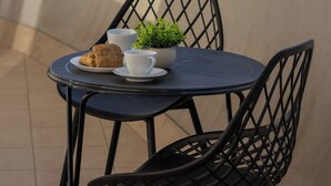 Ein Balkon mit Tisch, Stühlen, einem kleinen Topfpflanzen und einem Croissant.
