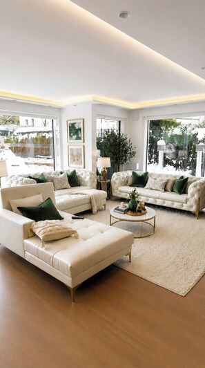 Ein geräumiges Wohnzimmer mit zwei weißen Sofas, einem Couchtisch und einem großen Fenster mit Blick auf Grünflächen.