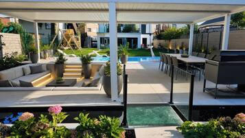 Eine überdachte Terrasse im Freien mit Pool, Sitzbereich und Grillstation.