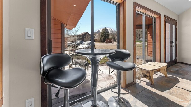 Ein modernes Interieur mit Glastür zum Patio, einem runden Tisch, zwei Barhocker und einem kleinen Holztisch.