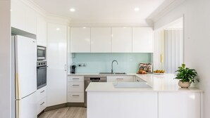 Uma cozinha moderna com armários brancos, forno embutido, lava-louças e uma pia.