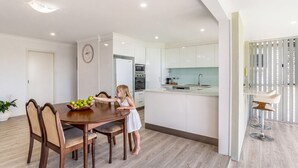 Uma cozinha moderna com armários brancos, uma mesa de jantar com cadeiras e um relógio na parede.