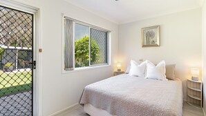 Quarto com cama, duas luminárias de cabeceira, janela com vista e porta com tela de segurança.