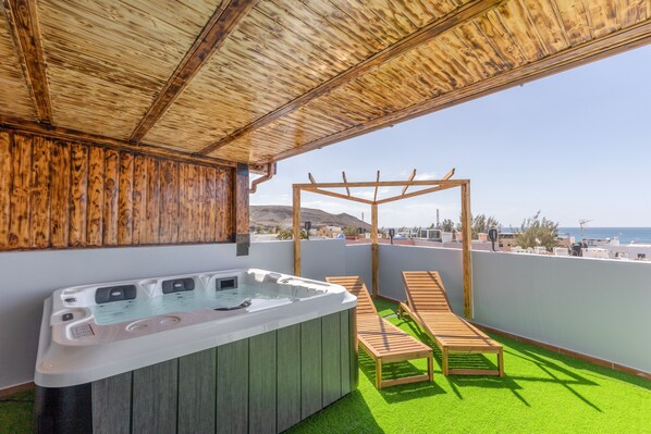 Terraza en la azotea con jacuzzi, sillones de madera y una pérgola.