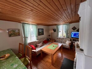 A cozy living room with a wooden ceiling, a sofa, a dining table, and a television.