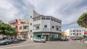 Ein mehrstöckiges Gebäude mit einem Geschäft im Erdgeschoss, einem sichtbaren Schild für 'Apartamentos Lobo' und mehreren parkenden Autos auf der Straße.