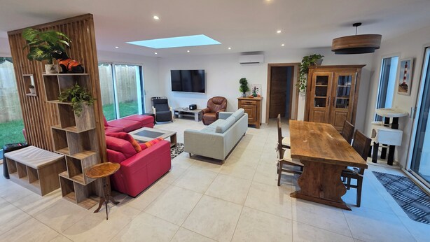 Una sala de estar moderna con un televisor grande, un comedor con una mesa de madera y un sofá rojo.