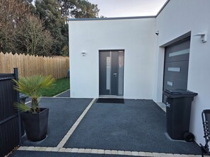 Una casa moderna con un garage, un cancello, un piccolo giardino e un bidone dei rifiuti.